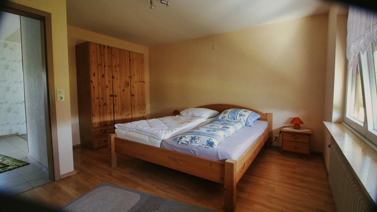 Ein einfaches Schlafzimmer mit einem Doppelbett und einem Holzkasten. Die Wände sind in sanften Farben gestrichen und es gibt einen kleinen Nachttisch.