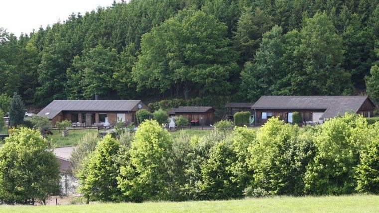 Gemütliche Hütten umgeben von grünen Bäumen in einer ländlichen Umgebung. Die Landschaft ist friedlich und einladend.