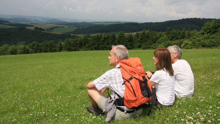 Trois personnes sont assises sur une pelouse avec vue sur un paysage vallonné.