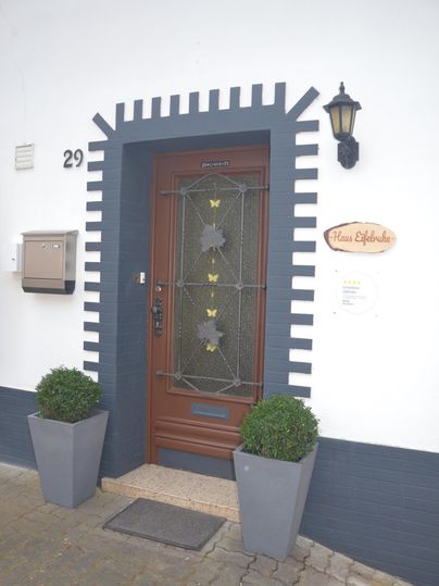 Een elegante voordeur met een mooi naambord. Aan beide zijden staan grote grijze plantenpotten.