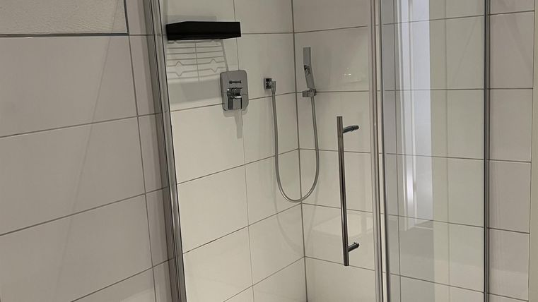 Een moderne douche met glazen afscheiding en uitnodigend design. De vloer is versierd met kleurrijke kiezels.