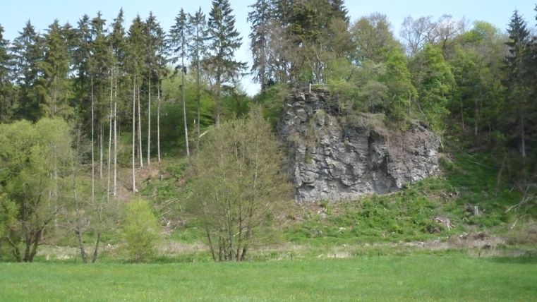 Felsformation am Waldrand mit grüner Wiese im Vordergrund.