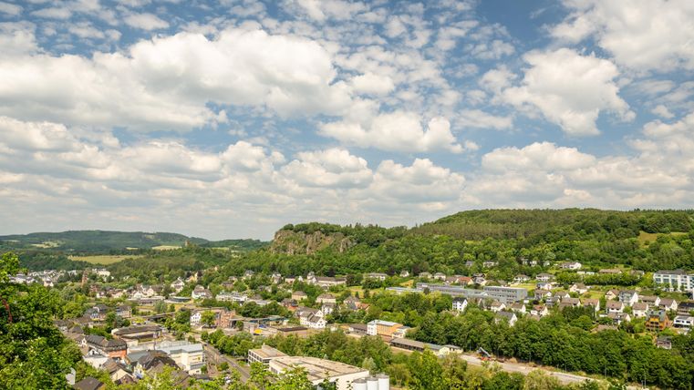 Eine malerische Landschaft mit einer kleinen Stadt und grünen Hügeln im Hintergrund. Der Himmel ist blau mit vielen weißen Wolken.