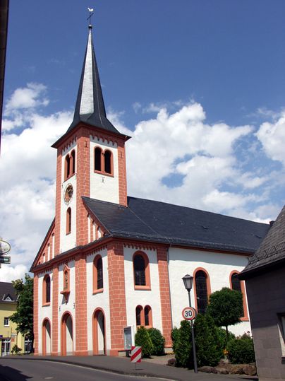 Kirche St. Josef in Stadtkyll mit spitzem Turm und blauem Himmel.