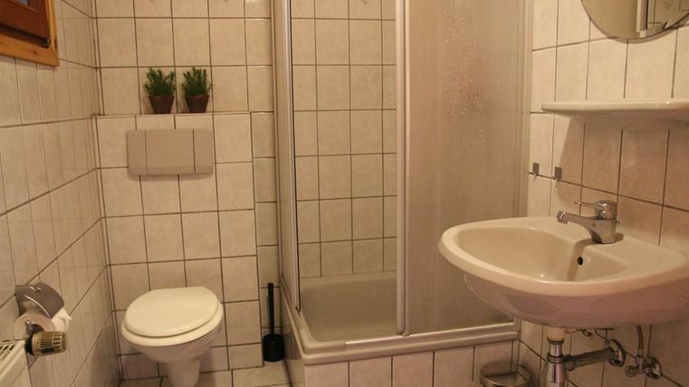 Ein kleines Badezimmer mit Dusche, Waschbecken und Toilette. Die Wände sind gefliest und es gibt zwei Pflanzen zur Dekoration.
