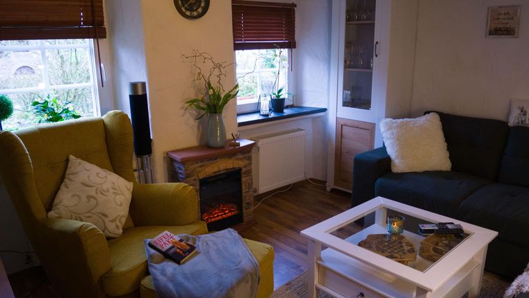 Een gezellige woonkamer met een gele stoel en een groene bank. De tafel van wit hout en de open haard geven de ruimte een uitnodigende sfeer.