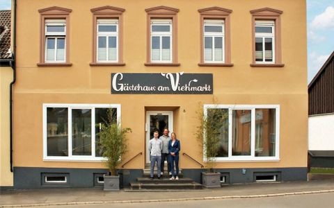 Een gastenhuis met twee personen voor de ingang. De gevel is in warme kleuren uitgevoerd en heeft grote ramen.