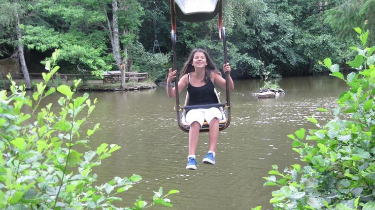 Ein Mädchen schwingt fröhlich über einem Teich. Umgeben von Bäumen und grünen Pflanzen genießt sie den Moment.