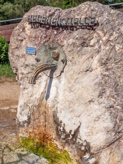 Stein mit Inschrift 'Helenenquelle' und Wasserhahn, aus dem Wasser tropft.