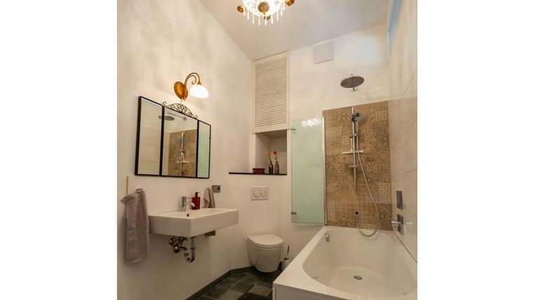 Ein modernes Badezimmer mit einer Badewanne, einer Dusche und einem eleganten Waschbecken. Die Wände sind hell, und es gibt einen schönen Kronleuchter.