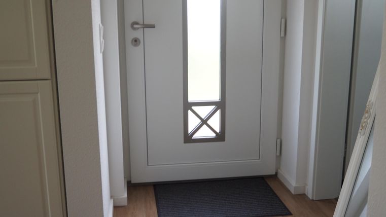 Ein moderner Eingangsbereich mit einer weißen Haustür und einem großen Fenster. Vor der Tür liegt ein matten mit dem Spruch „Hearts to Huddle“.