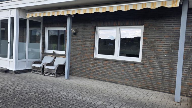 Une terrasse avec deux chaises et une cloison en pierre. Au-dessus de la terrasse se trouve un store.