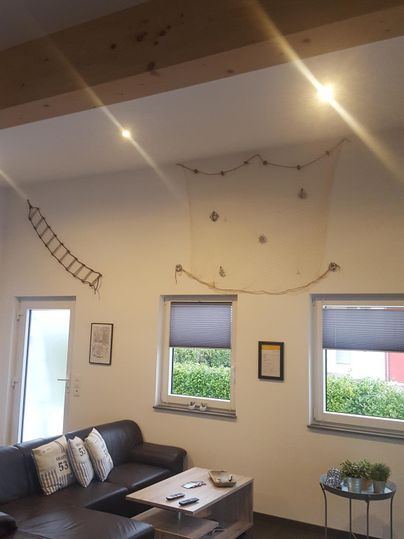 Ein modernes Wohnzimmer mit einer dunklen Couch und einem niedrigen Tisch. Helle Wände und schöne Fenster sorgen für ein einladendes Ambiente.