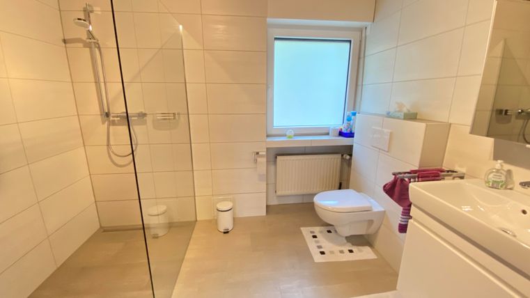 Ein modernes Badezimmer mit Dusche und großer Fenster. Die Wände sind weiß gefliest, und es gibt eine elegante Waschbeckenanlage.