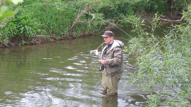 Mann steht in der Kyll mit einer Angel in der Hand