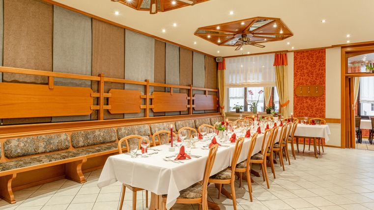 Ein eleganter Speisesaal mit langen Tischen, die festlich gedeckt sind. Die Wände sind mit Holzpaneelen und dekorativen Elementen gestaltet.