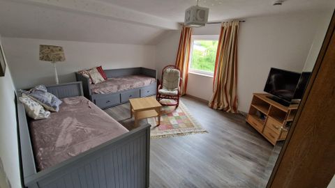 Ein gemütliches Zimmer mit zwei Betten, einem Tisch und einem Stuhl. Durch das Fenster fällt viel Tageslicht und man sieht das Grün draußen.