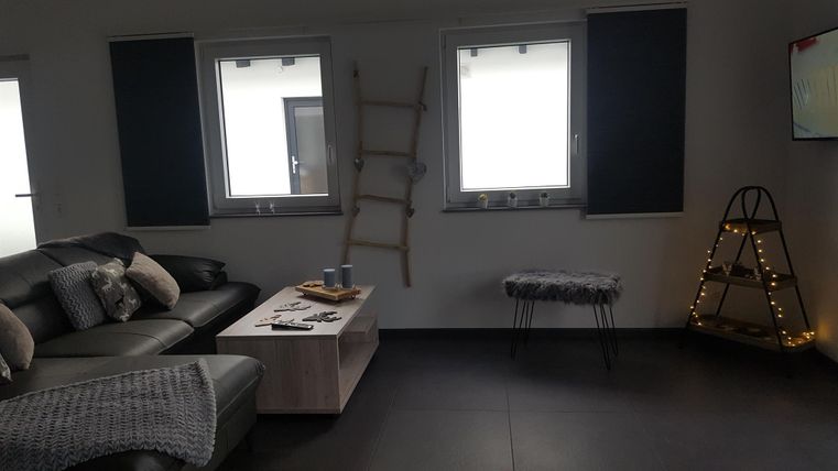 Ein moderner Wohnraum mit einer gemütlichen Couch und einem Couchtisch. An der Wand steht eine dekorative Leiter und es gibt Fenster mit Jalousien.