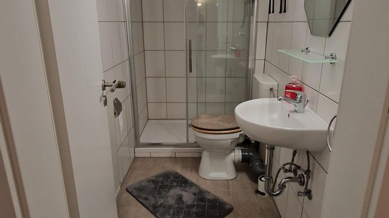 Une salle de bains moderne avec douche, lavabo et WC. Les murs sont carrelés et il y a un petit tapis sur le sol.