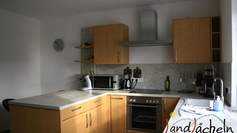 Eine moderne Küche mit Holzschränken und Edelstahlgeräten. Es gibt eine Arbeitsfläche aus Stein und Fensterlicht, das den Raum erhellt.