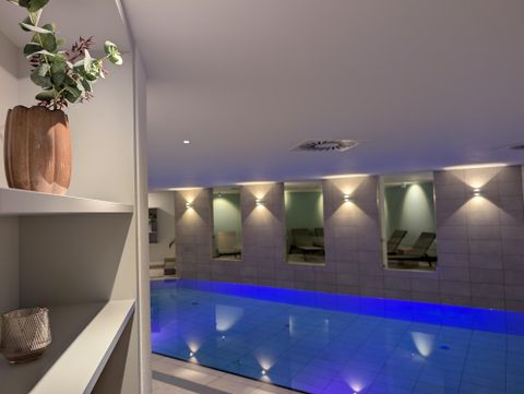 Ein Indoor-Pool mit blauem Wasser in einem warm beleuchteten Spa-Raum.