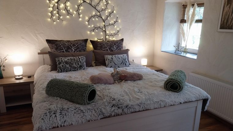 Een gezellige slaapkamer met een groot bed en decoratieve verlichting boven het hoofdeinde. De inrichting is modern en uitnodigend, met warme houttinten en zachte kleuren.