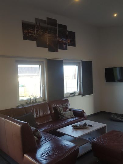 Ein modernes Wohnzimmer mit einer großen Couch und einem Couchtisch. An der Wand hängen mehrere Bilder, und ein Fernseher ist ebenfalls sichtbar.