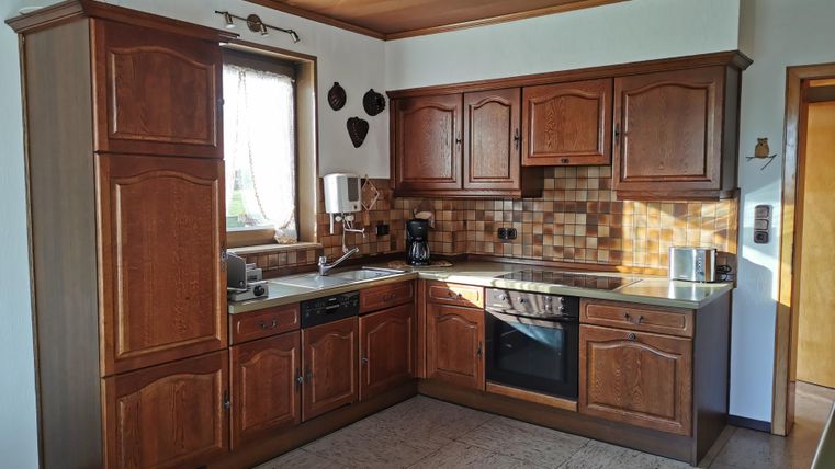 A modern kitchen with wooden cabinets and a bright tiled floor. It is equipped with a refrigerator, stove, and sink.
