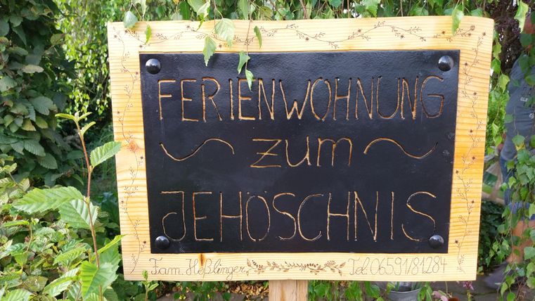 Een bord met de opschrift „Vakantiehuis tot Jehoschnis“. Het staat voor een groene, plantrijke omgeving.