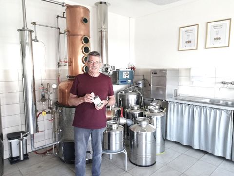 Ein Mann vor einer Destilliermaschine mit einer Flasche Gin in der Hand.