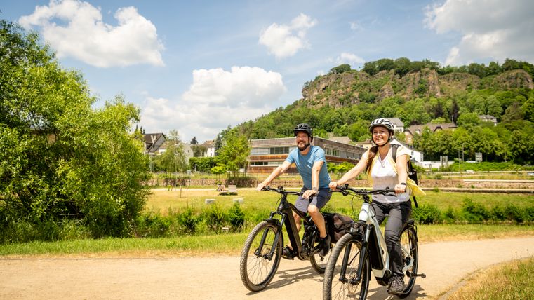 Zwei Personen fahren mit Fahrrädern auf einem Weg, umgeben von grüner Landschaft und Hügeln.