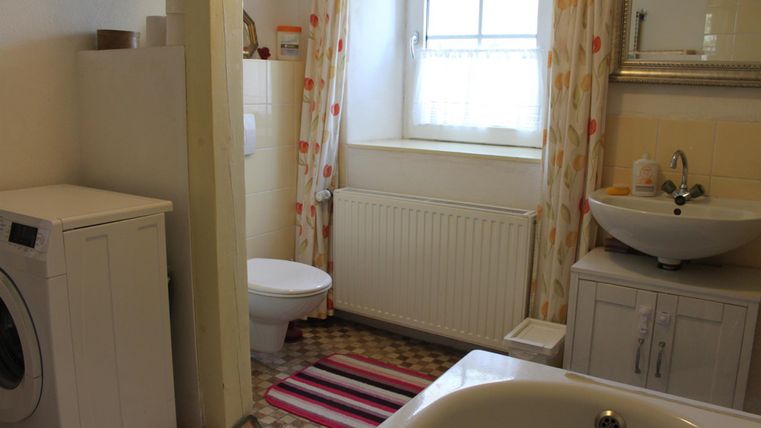 Een lichte badkamer met een wasmachine, een wastafel en een toilet. De muren zijn versierd met lichte gordijnen en een tapijt zorgt voor een gezellige accent.