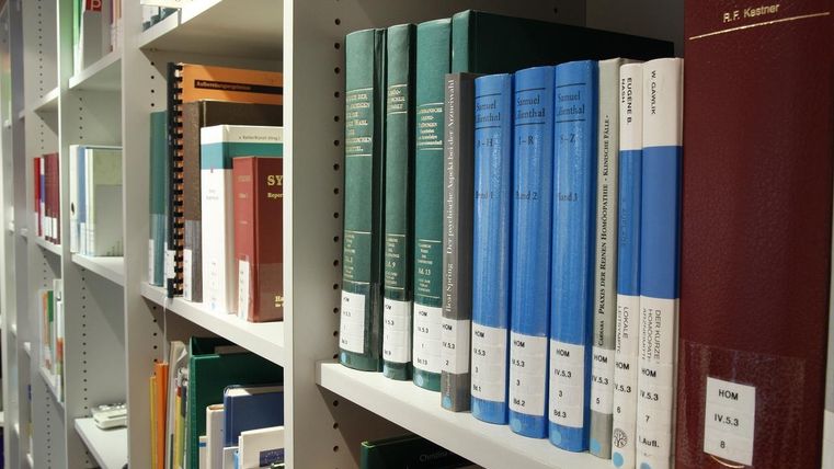 Symbolbild- Ein Bücherregal in weißer Farbe. Darin aufgereiht sind viele Bücher in verschiedenen Größen und Farben.