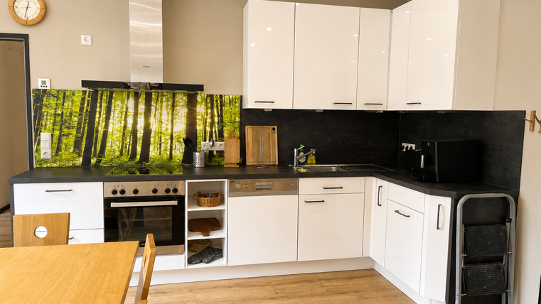 Une cuisine moderne avec des placards blancs et un espace de travail sombre. En arrière-plan, il y a un revêtement mural saisissant avec un motif forestier.
