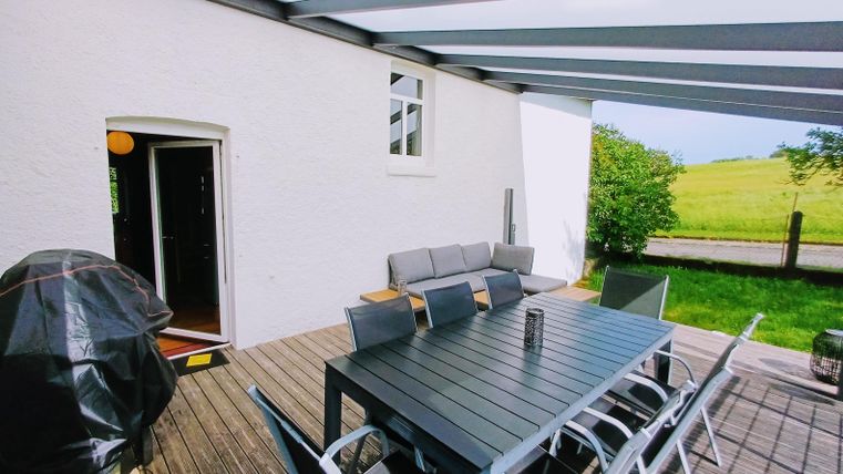 Une terrasse moderne avec une grande table à manger et des chaises confortables. En arrière-plan se trouve une pelouse verte et luxuriante.