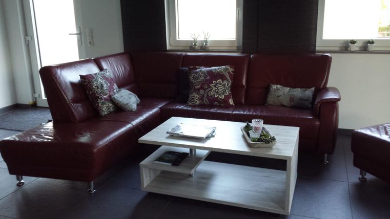 Ein modernes Wohnzimmer mit einer roten Ledercouch und einem weißen Couchtisch. Auf dem Tisch liegen einige Dekorationsartikel und die Fenster lassen viel Tageslicht herein.