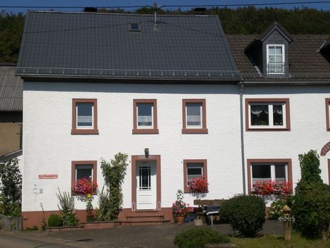Ein weisses Haus mit roten Fensterrahmen und einer Solaranlage auf dem Dach. Vor dem Haus stehen blühende Pflanzen und ein kleiner Garten.