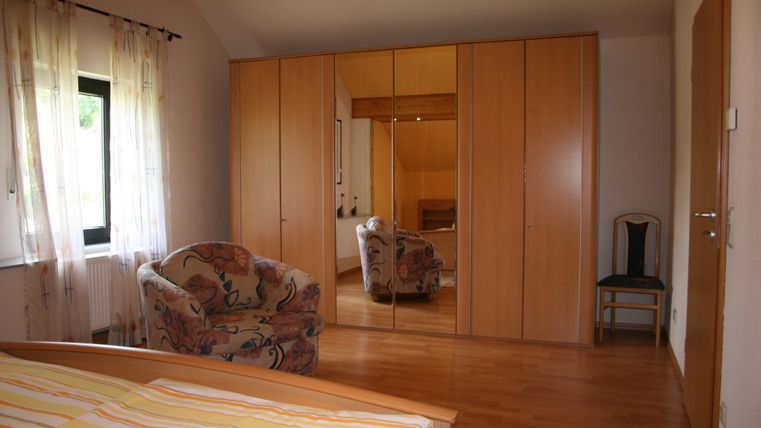 Ein gemütliches Schlafzimmer mit einem großen Spiegelschrank und einem bequemen Sessel. Das Licht fällt durch die Fenster und schafft eine einladende Atmosphäre.