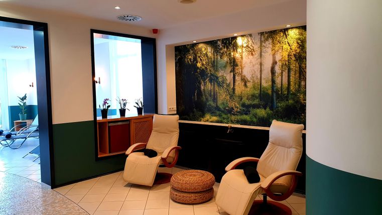 A quiet reception area with two comfortable armchairs and a forest wallpaper. The floor is bright tiled and creates a relaxed atmosphere.