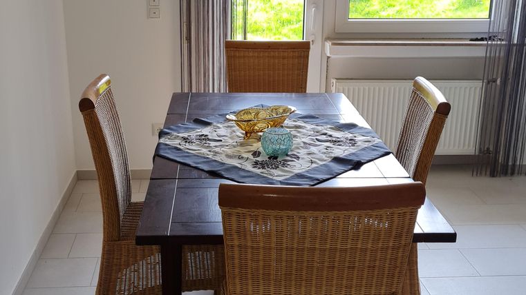 A bright dining area with a wooden table and rattan chairs. Large windows provide plenty of daylight and a view of the greenery.