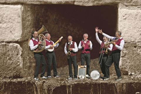 Gruppenbild der Musiker. Einzelne spielen auf ihren Instrumenten andere jubeln.