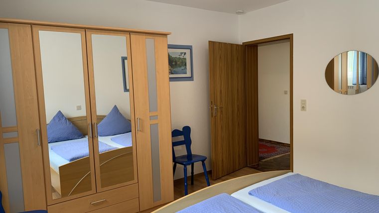 Ein einfaches Schlafzimmer mit zwei Einzelbetten und blauen Decken. Es gibt einen großen Kleiderschrank und einen Spiegel an der Wand.