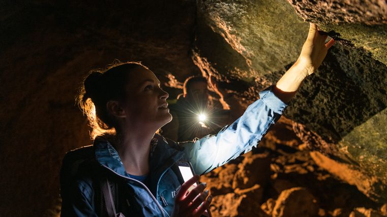 Personne dans une grotte avec une lampe de poche qui examine le plafond.