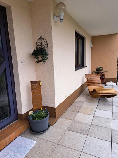 Ein einladender Eingangsbereich mit einer Liege aus Holz und einem Blumenpflanzer. Die Wände sind hell gehalten und es gibt eine dekorative Wandhängung.