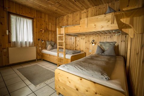 Une chambre confortable avec des panneaux en bois. Il y a un lit superposé et un lit simple, tous deux avec une literie simple.