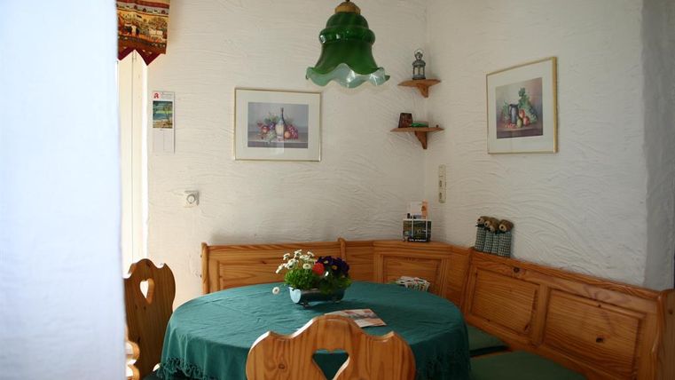 Een gezellige eetruimte met houtkleurige banken en een ronde tafel. Aan de muren hangen schilderijen, en een groene lamp zorgt voor sfeervolle verlichting.