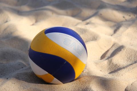 Ein blau, gelb und weiß gestreifter Volleyball liegt auf einer Sandfläche.