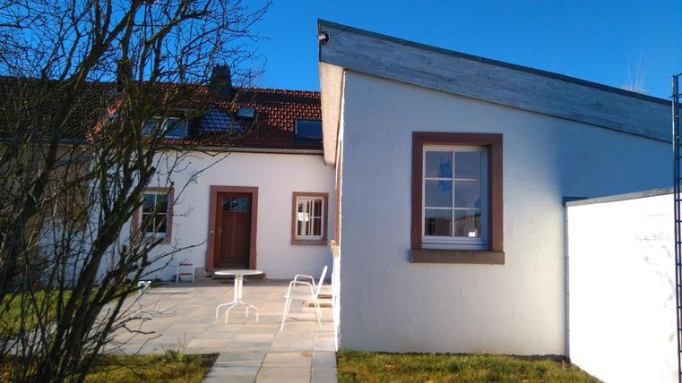Een modern huis met een lichte buitenruimte en een zithoek. De lucht is helder en blauw.