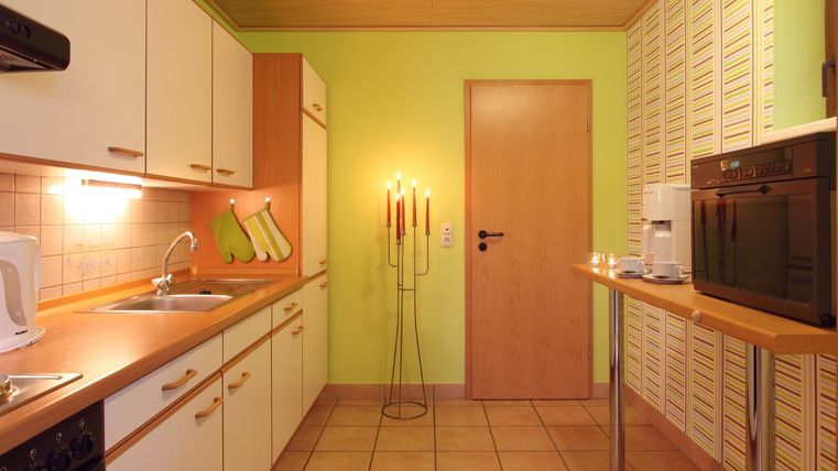 Eine gemütliche Küche mit grünen Wänden und Holzregalen. Auf dem Tisch stehen Kerzen und ein moderner Kaffeemaschine.