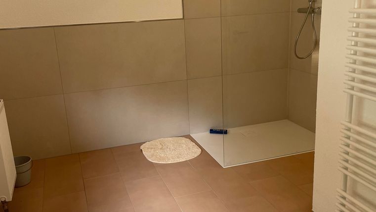 Une salle de bains moderne avec une douche et une baignoire. Le sol est carrelé en brun, et il y a un porte-serviettes au mur.